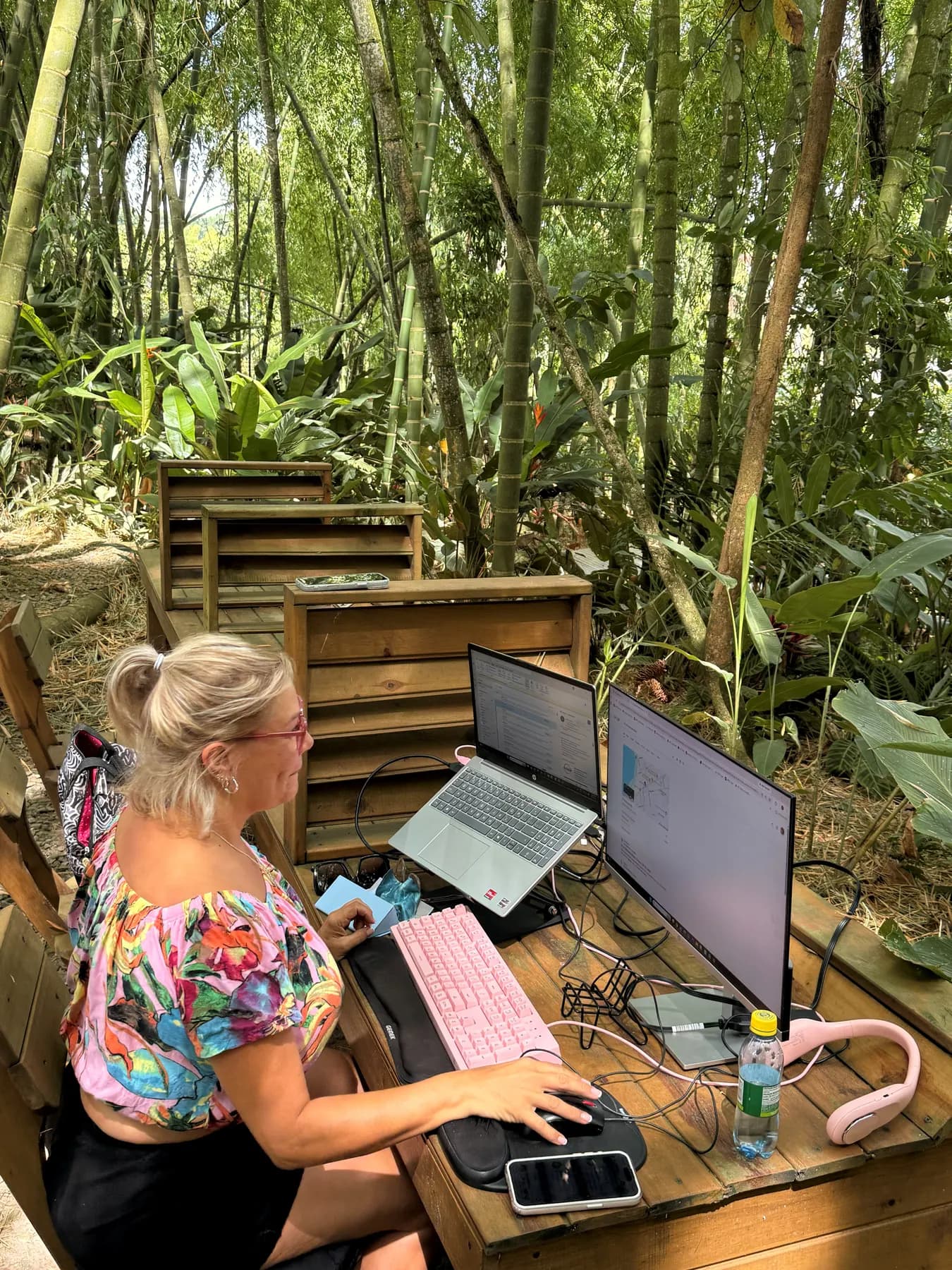 Person working on a laptop at a wooden desk inside the bamboo forest