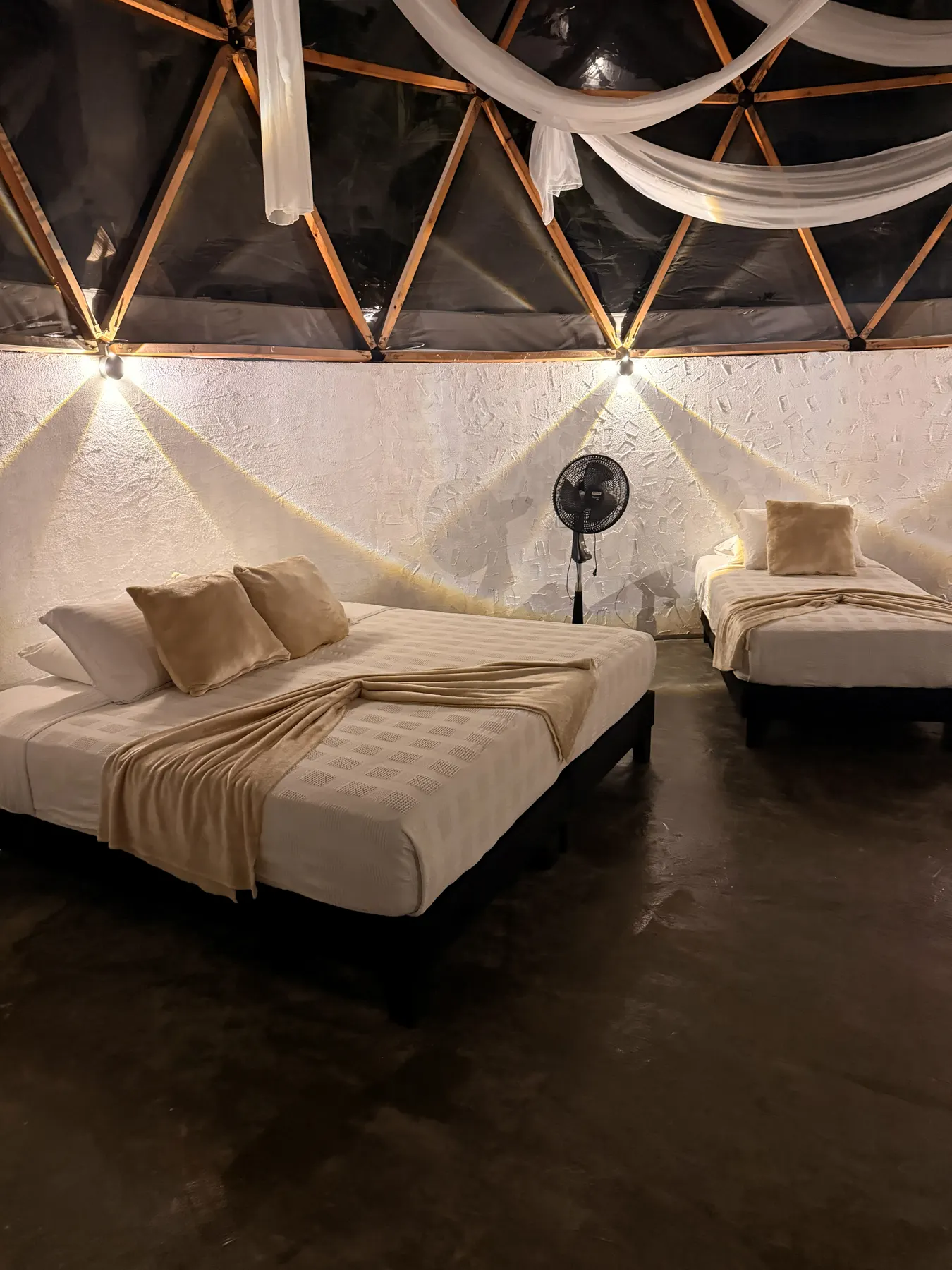 The dome’s beds at night, warm light on the walls and a standing fan