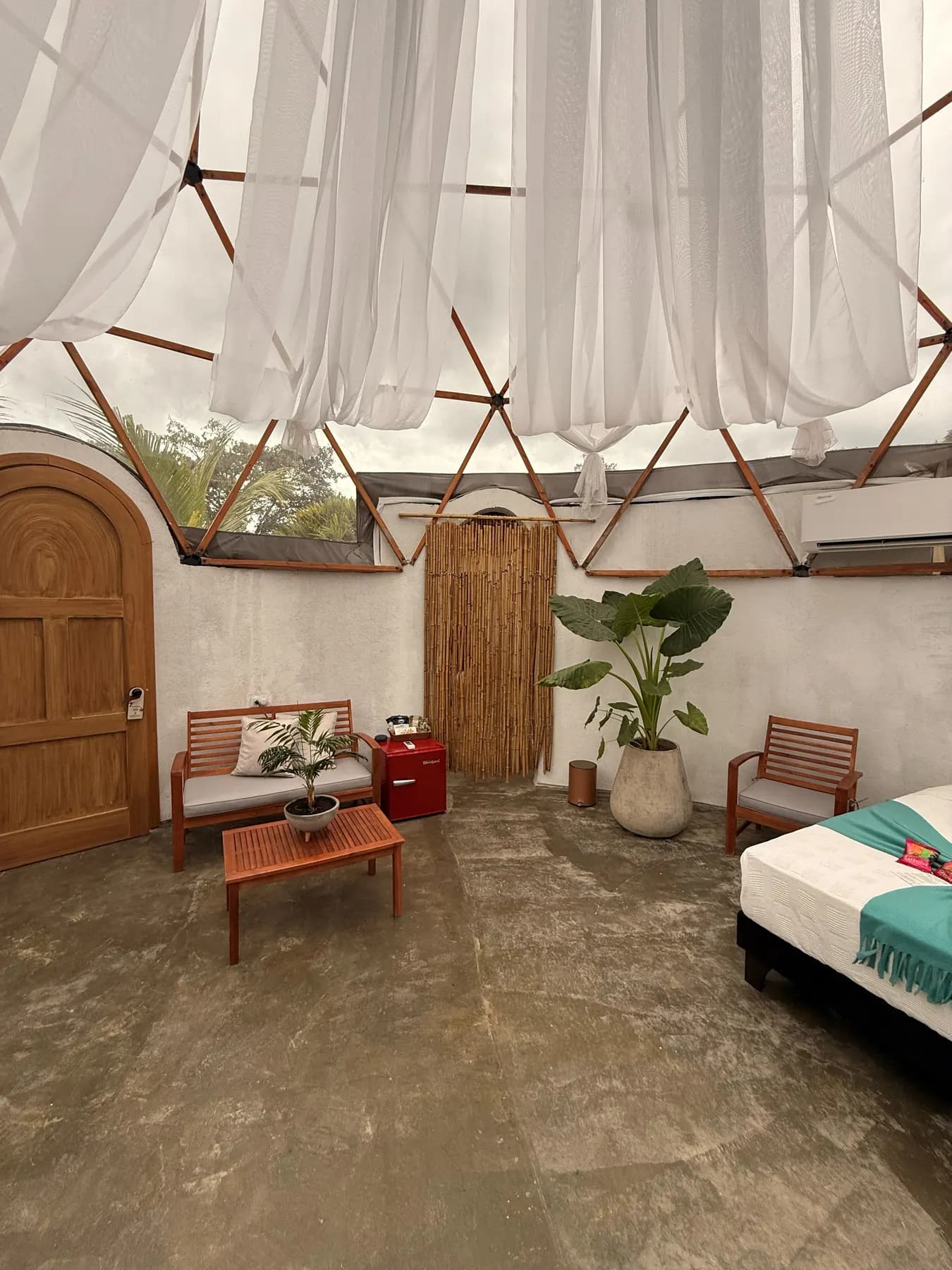 A corner of the dome with a wooden sofa, a red trunk and a plant beside the arched door