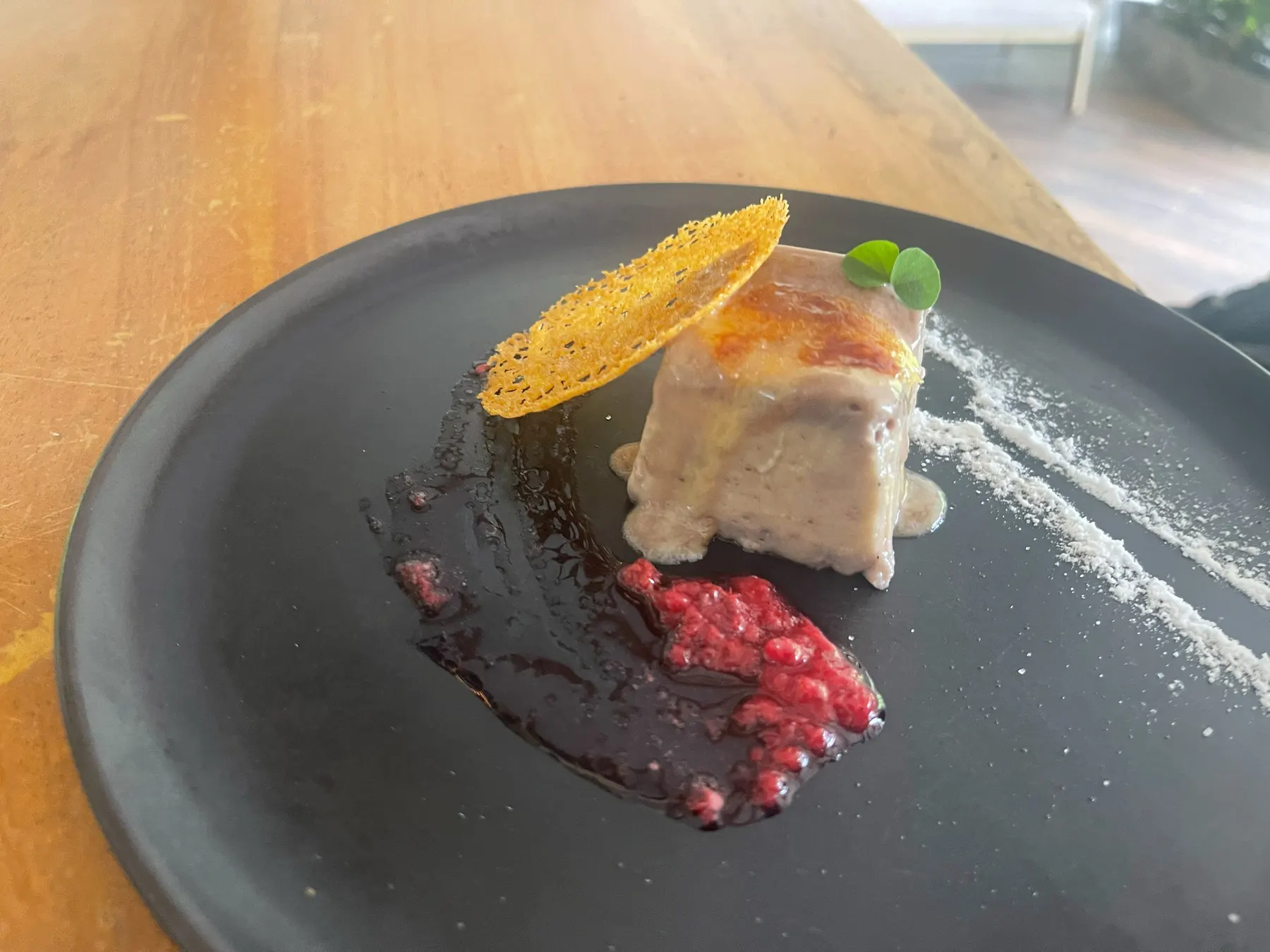 Dark plate with a portion of fish, a line of sauce and an edible flower