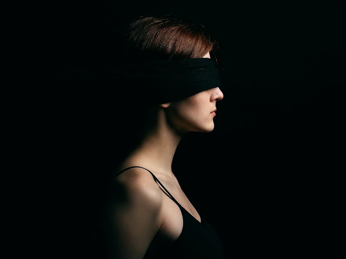 A blindfolded woman against a black ground