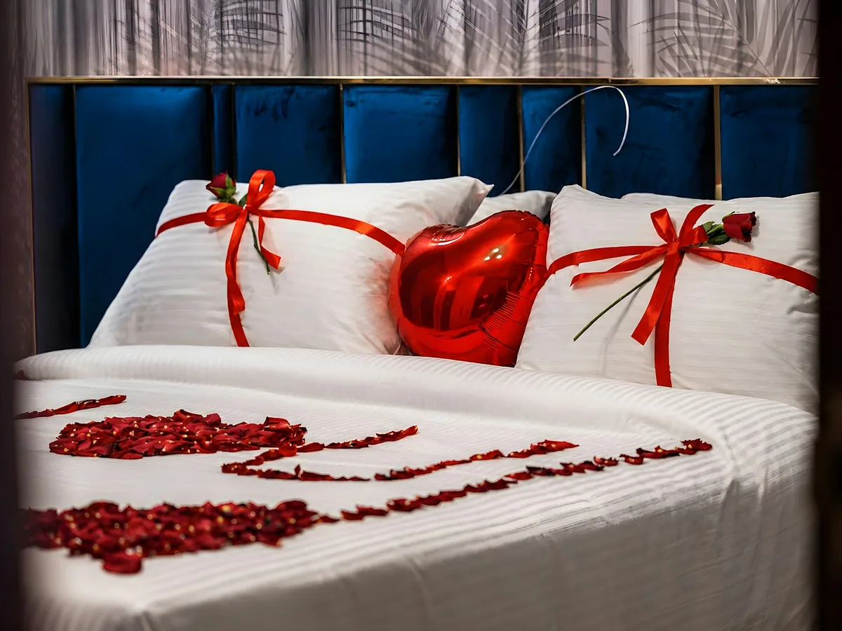 A bed decorated with rose petals and red cushions