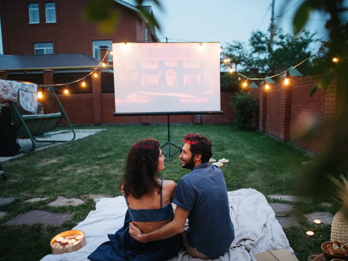 A couple watching a film on an outdoor screen under string lights