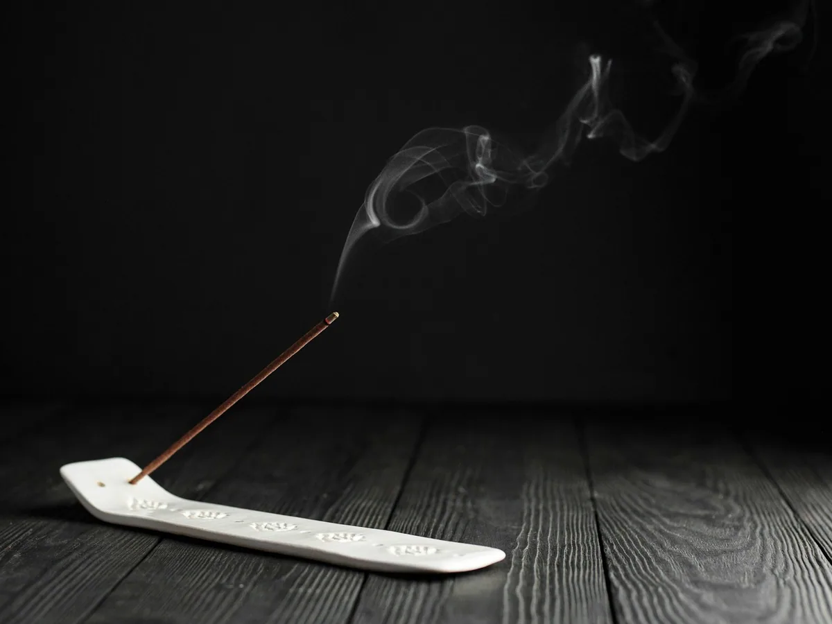 A lit incense stick with smoke on wood