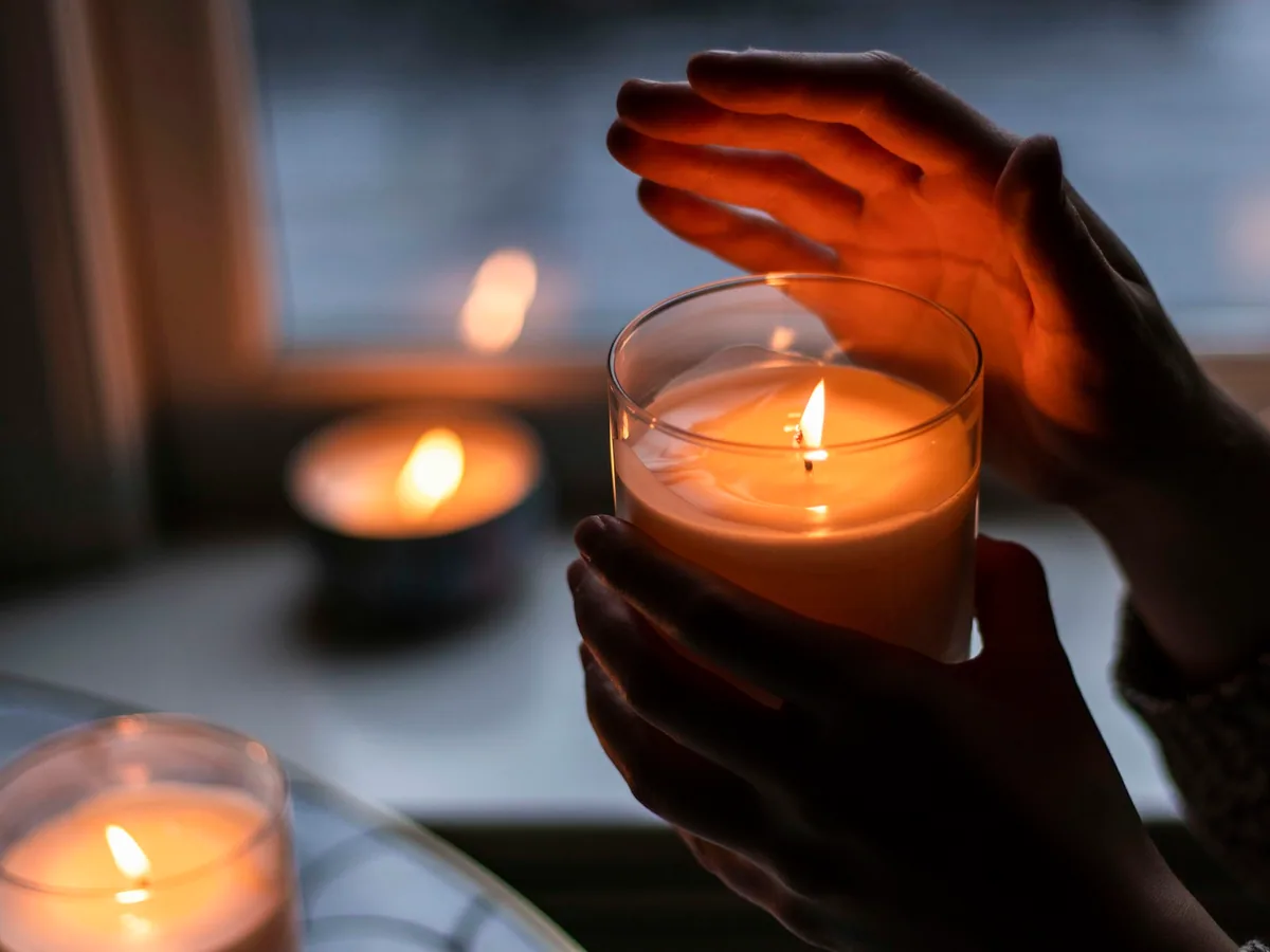 Hands over a lit candle in low light