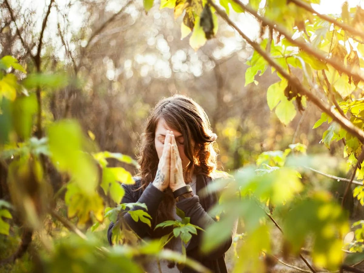 A woman with her hands together meditating among leaves
