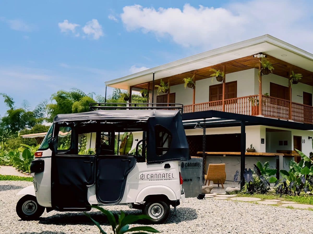 A black-and-white tuk tuk carrying the Cannatel logo, parked in front of the hotel building
