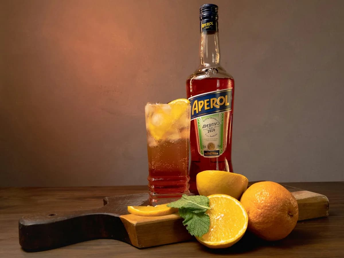 A bottle of Aperol beside a spritz and oranges