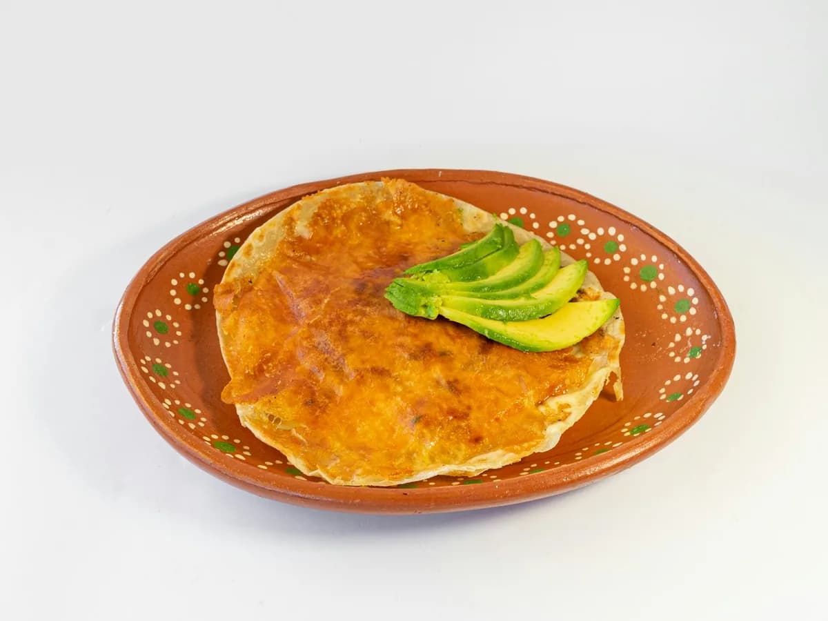An arepa with cheese and avocado slices on a clay plate