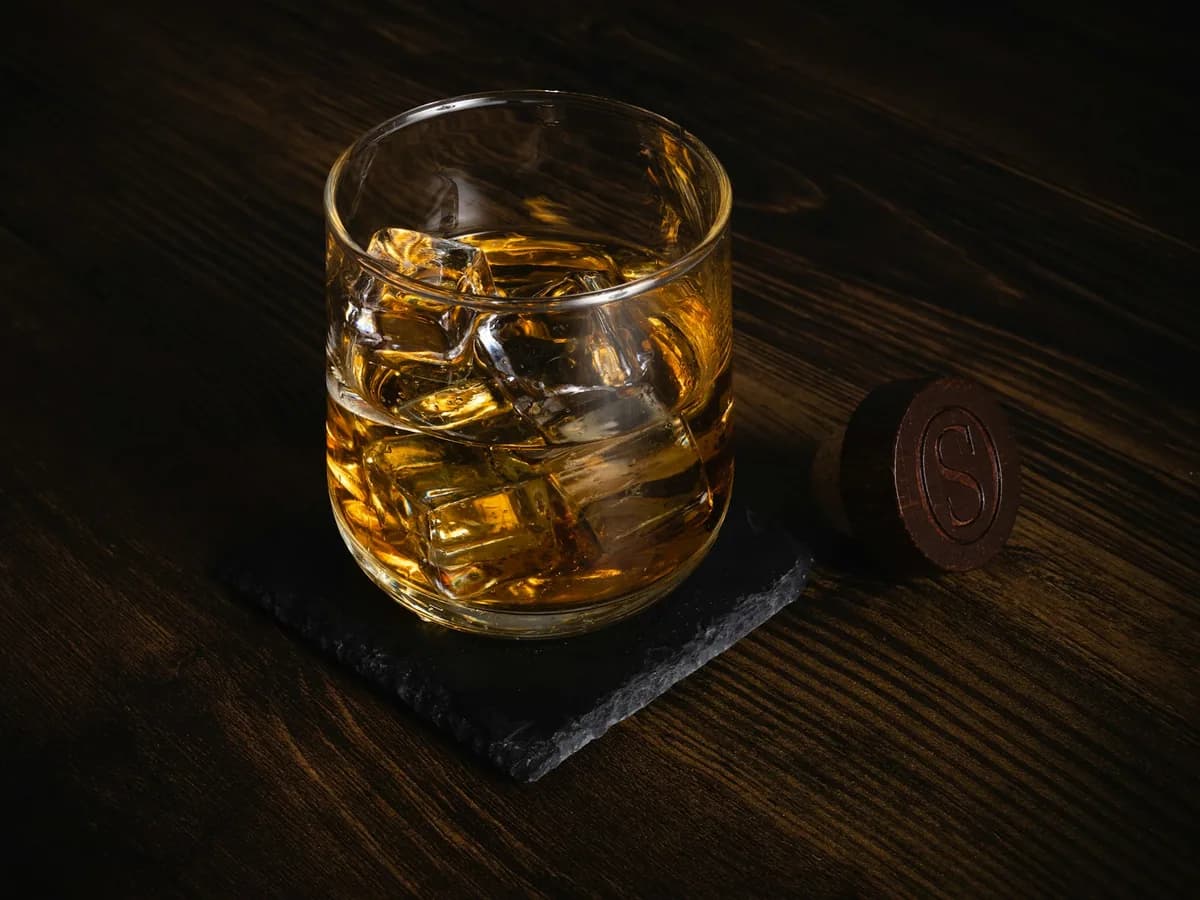A glass of whisky with ice on slate