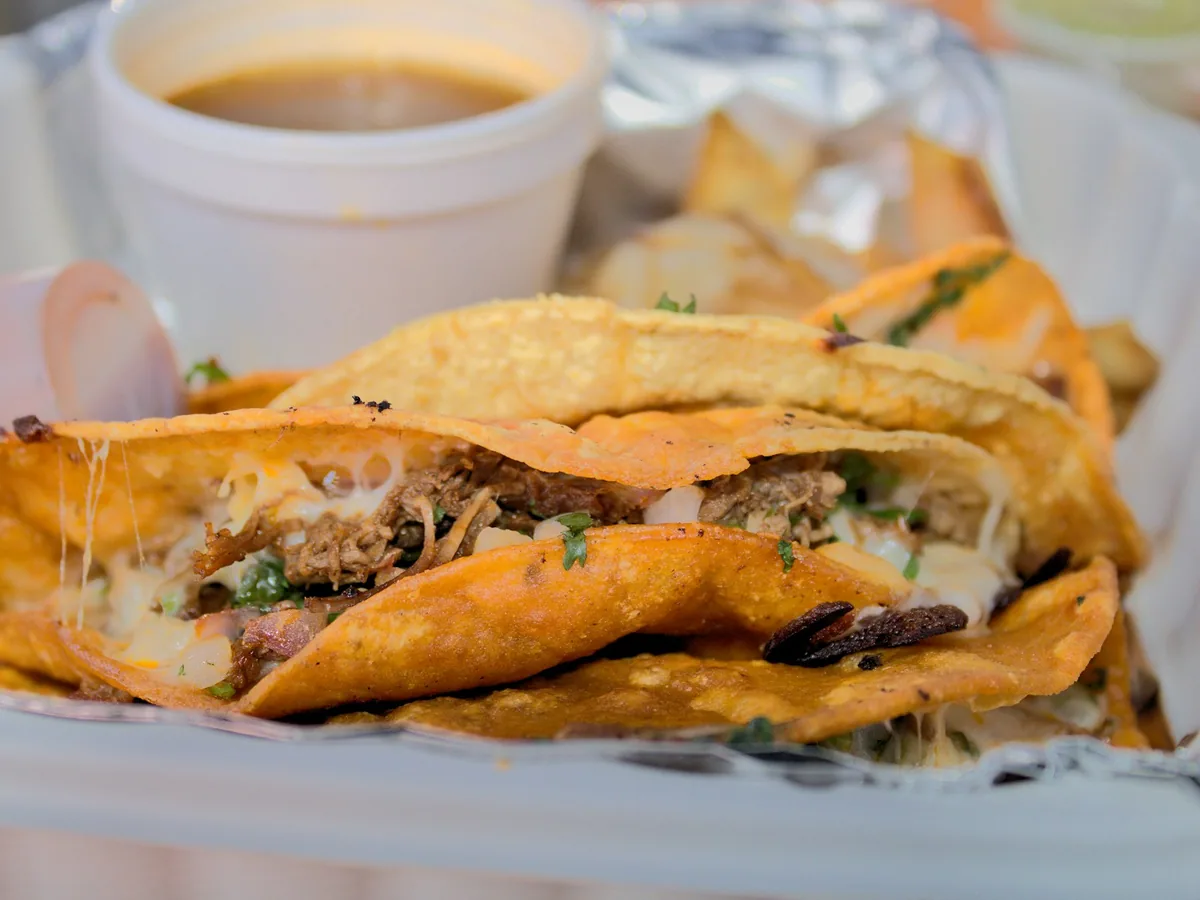 Birria tacos beside a cup of consommé