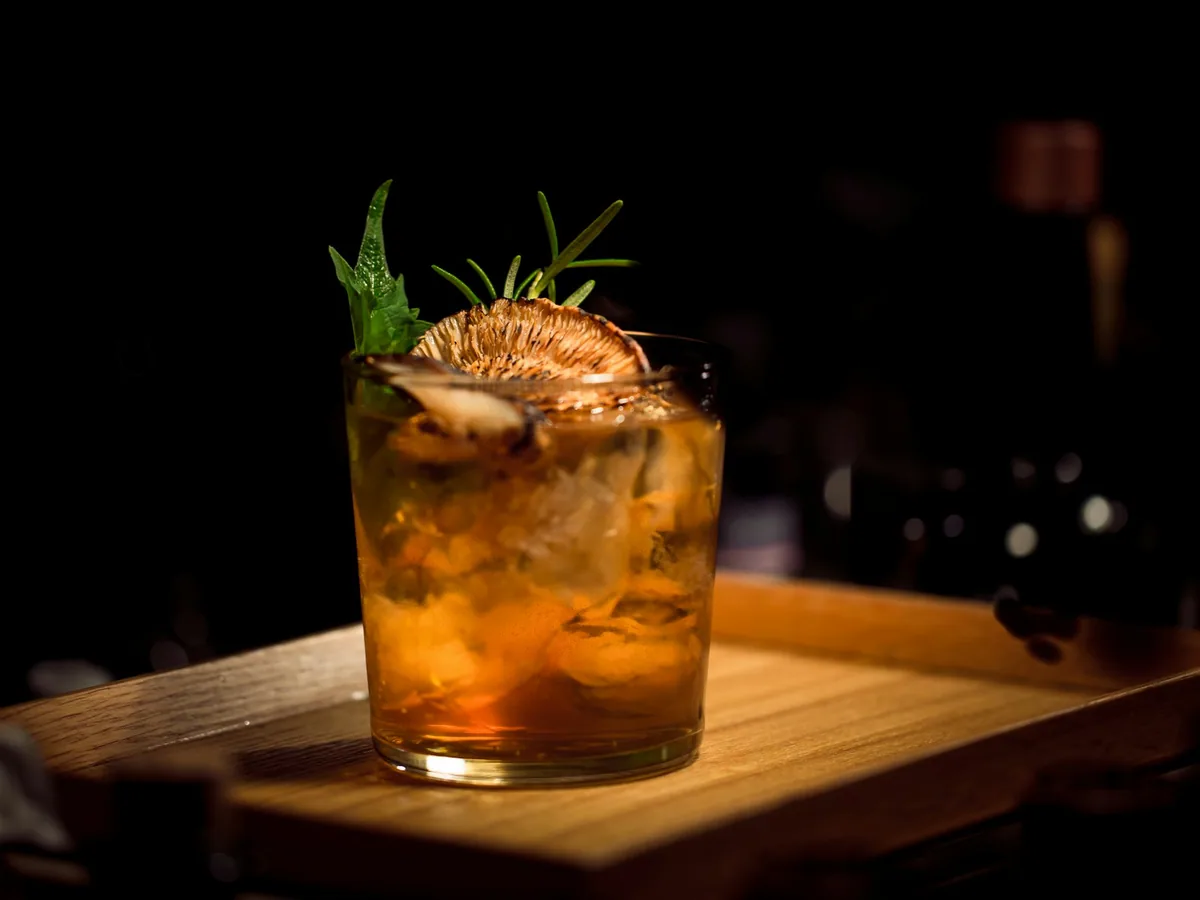 An amber cocktail with ice and herbs in a short glass
