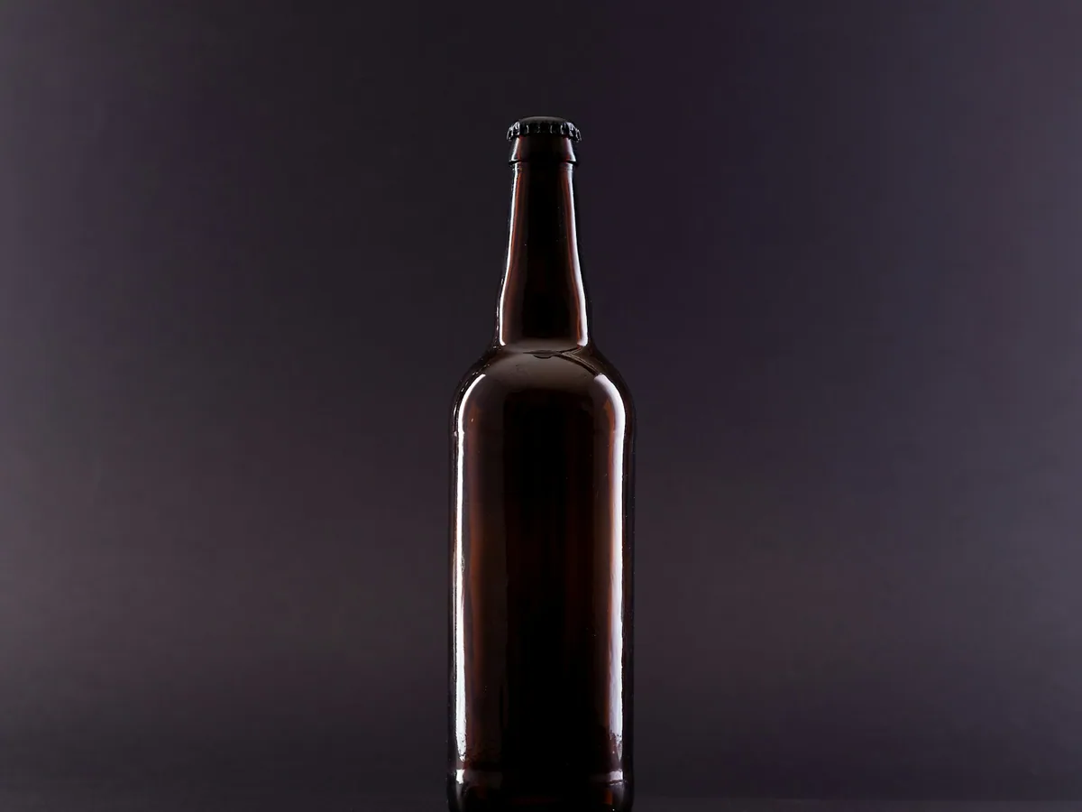 A dark beer bottle against a plain ground