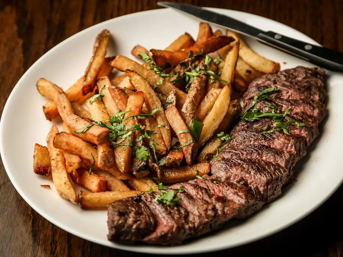 A grilled steak with fried potatoes and herbs on a plate