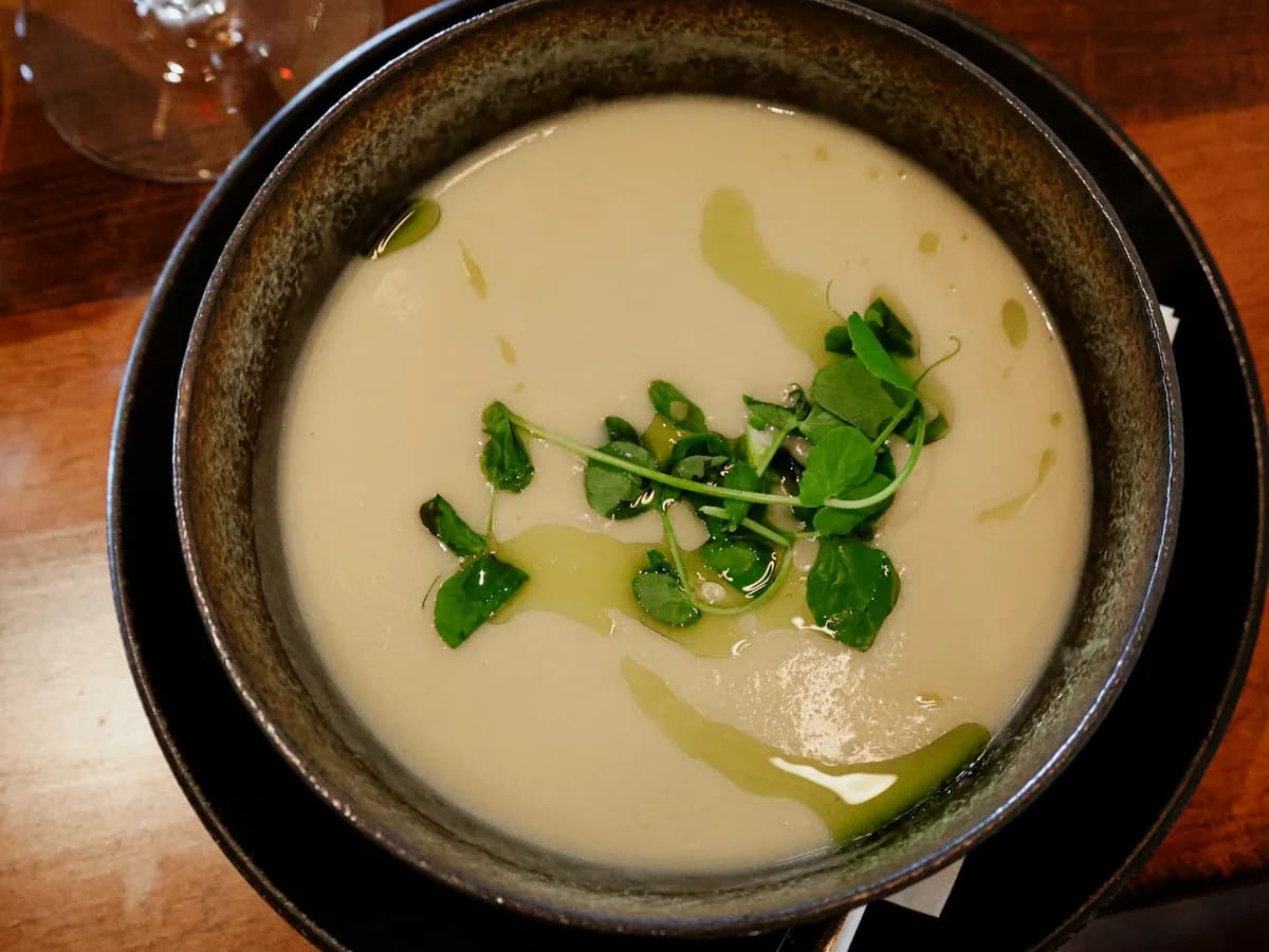 A cream soup in a dark bowl with fresh herbs and a thread of oil