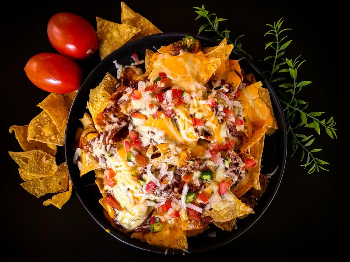 Nachos with cheese and tomato in a black bowl