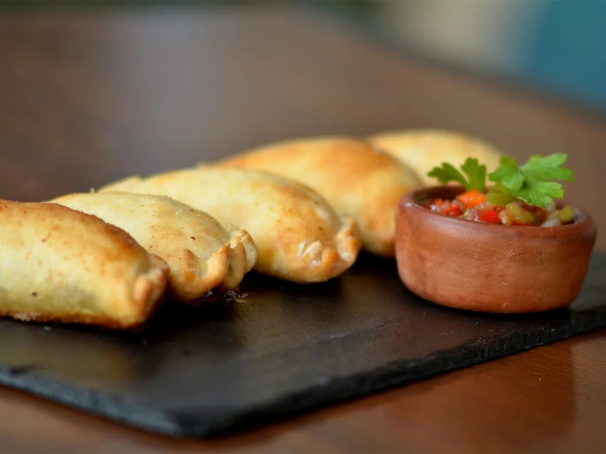 Golden empanadas on a slate board with a small bowl of salsa