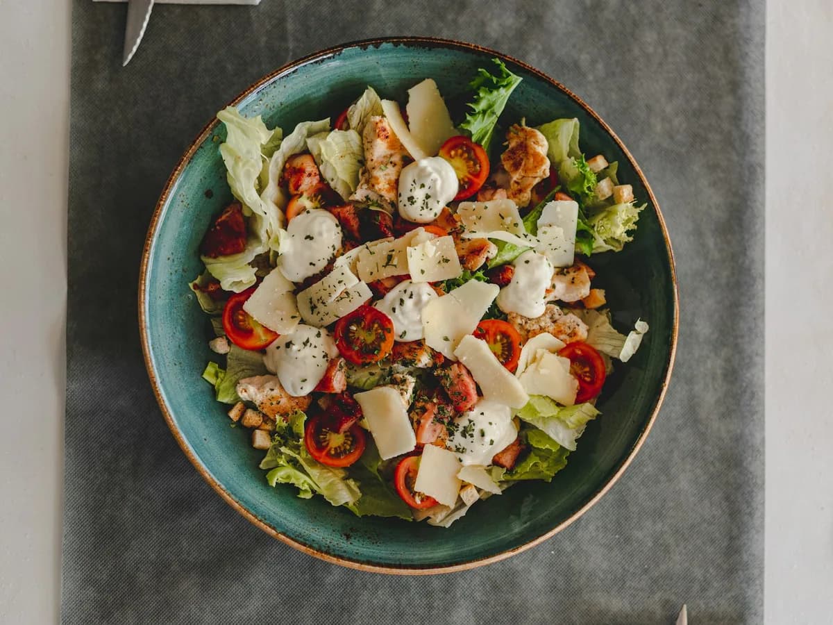 A salad with chicken, tomato and cheese in a green bowl