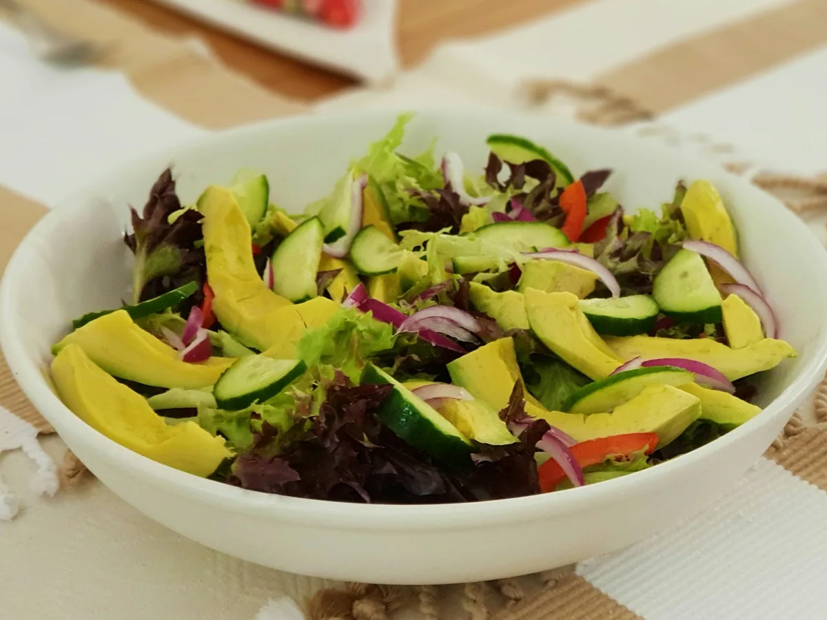 A green salad with avocado in a white bowl