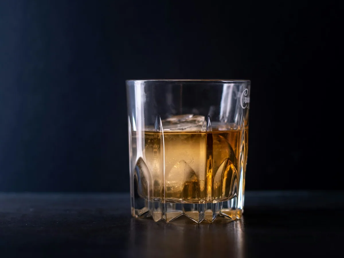 A glass of whisky with ice against a dark ground