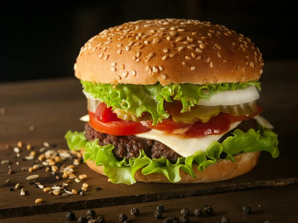 A beef burger with lettuce, tomato and cheese against a dark ground