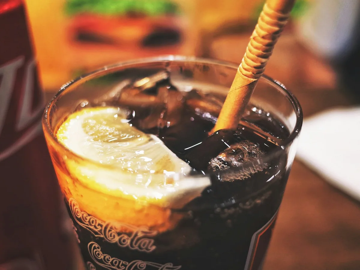 A tall glass of cola cocktail with ice and lemon