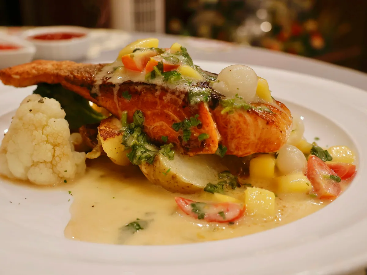 Salmon in sauce with sautéed vegetables on a white plate