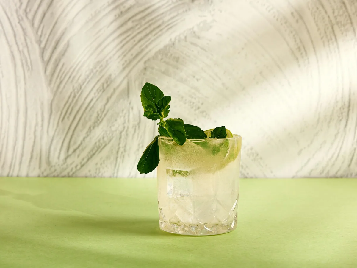 A mojito with mint and lime against a green ground