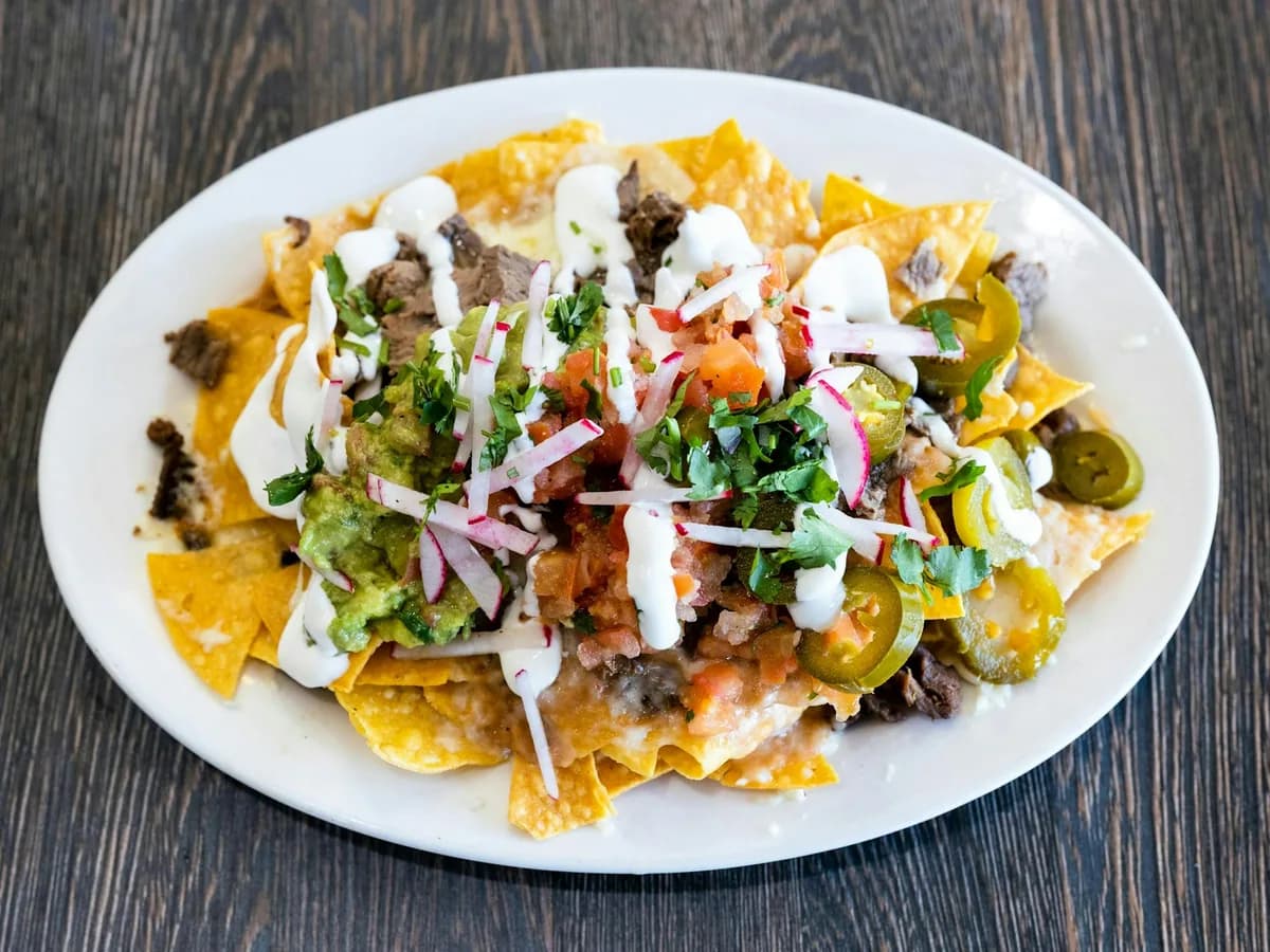 Nachos topped with meat, cheese and cream on a white plate