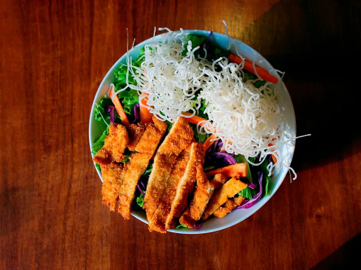 Grilled chicken strips over a salad in a bowl