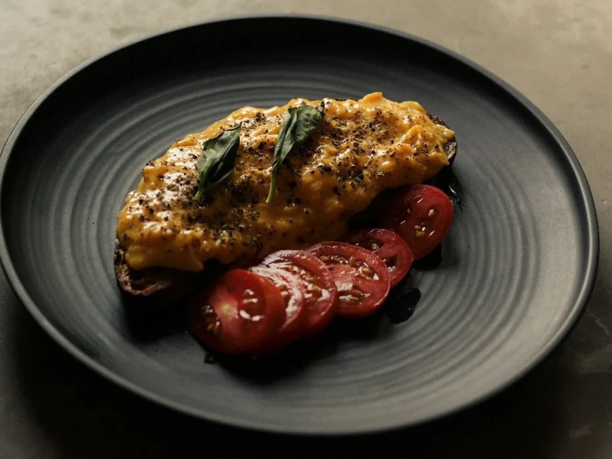 A chicken breast in sauce on a black plate
