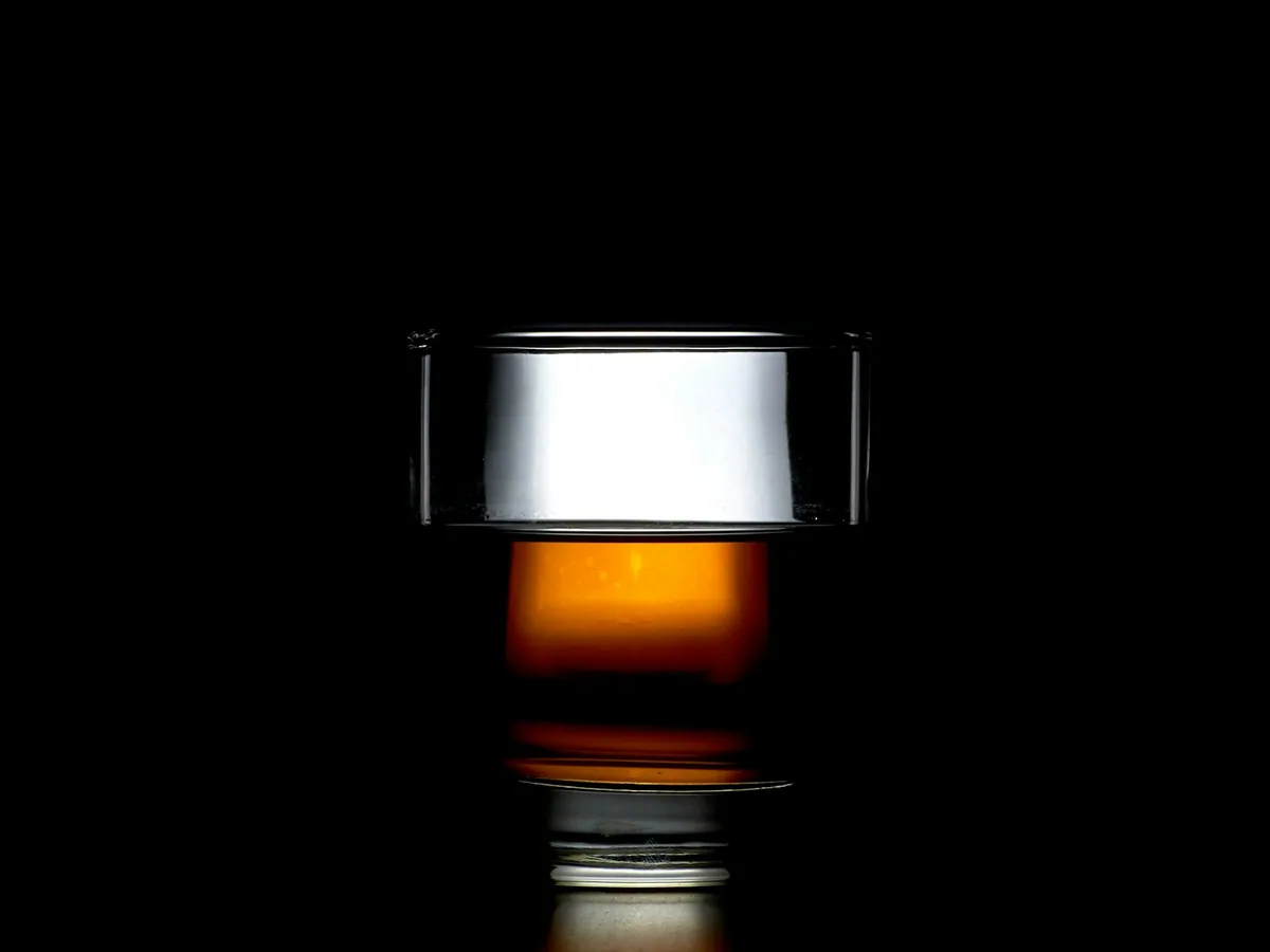 A glass of amber rum against a black ground