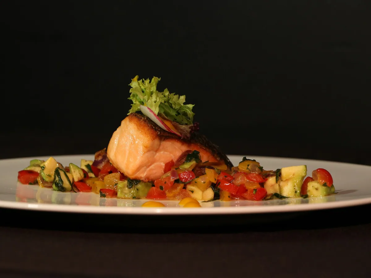 A plated salmon fillet with vegetables on a dark plate