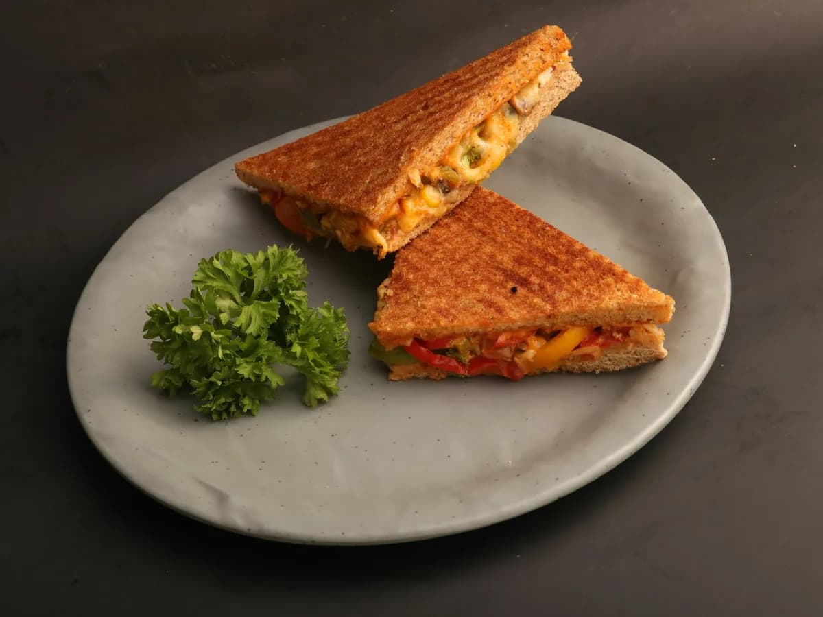 A toasted cheese sandwich on a grey plate with a sprig of parsley