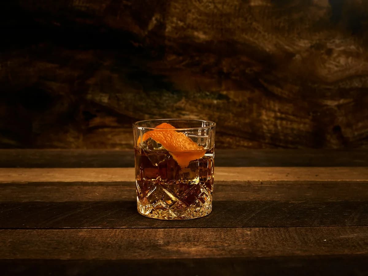 A short glass of whiskey with citrus peel on wood