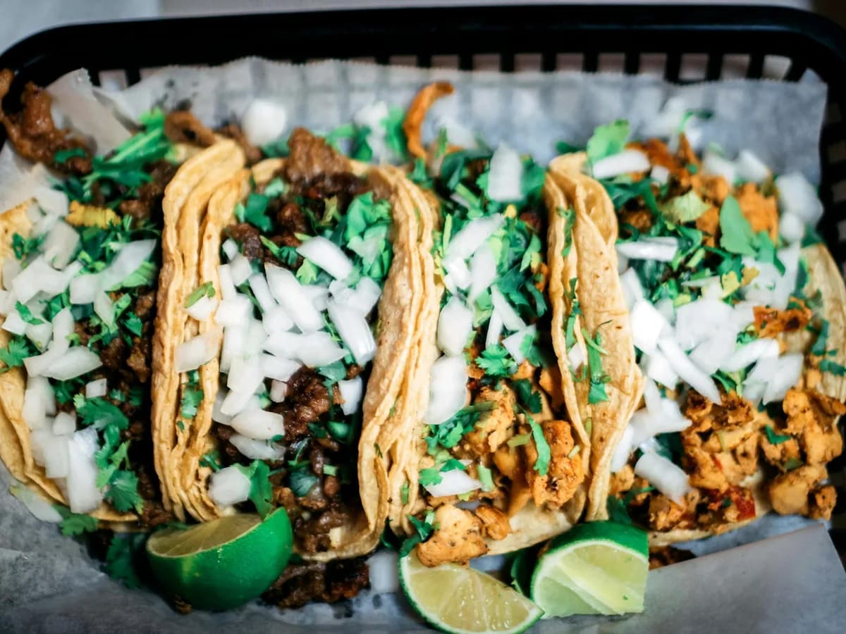 Three tacos with meat, onion and coriander on a board