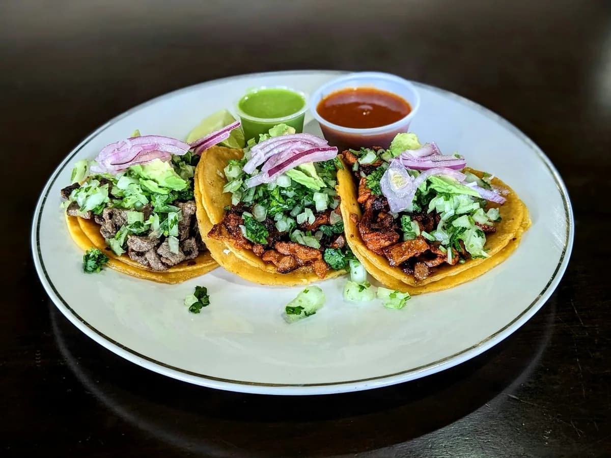 Three tacos with red onion and salsa on a white plate