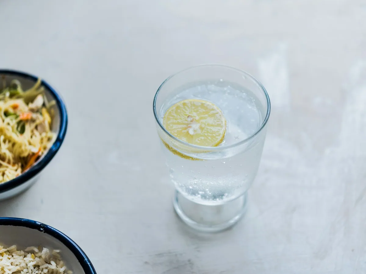 A tall glass with tonic, ice and a slice of lemon