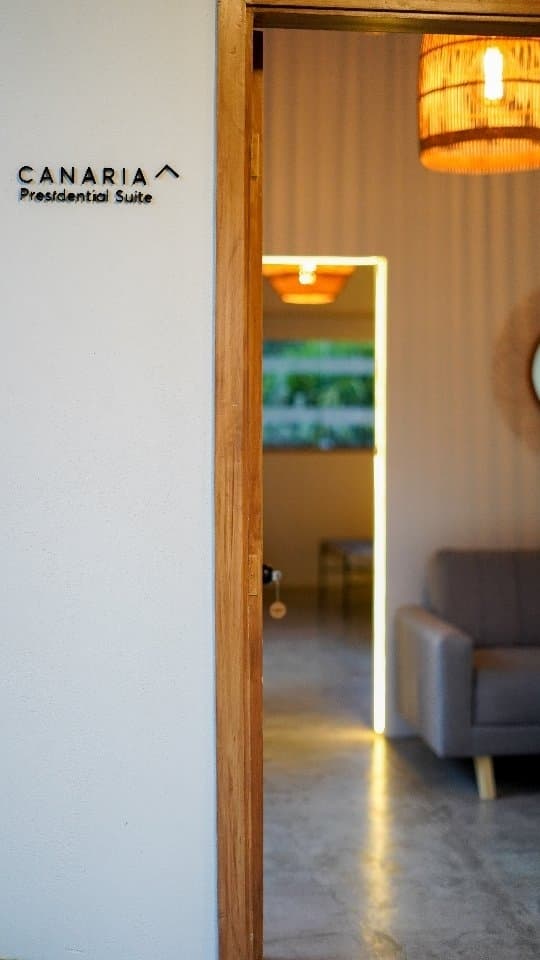 The open wooden door of the Canaria suite, the “Canaria, Presidential Suite” sign on the wall and a fibre lamp inside