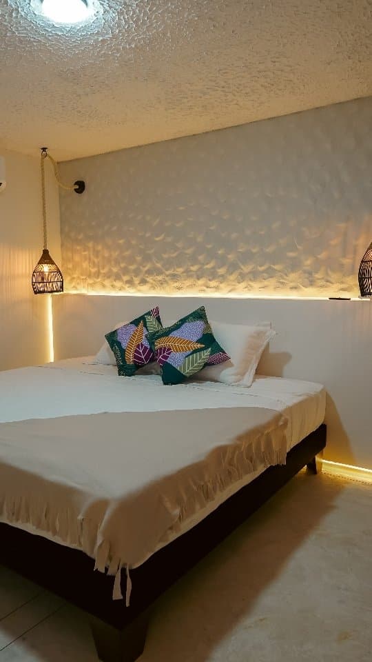 The La Bota room bed with a green throw and warm light at the headboard