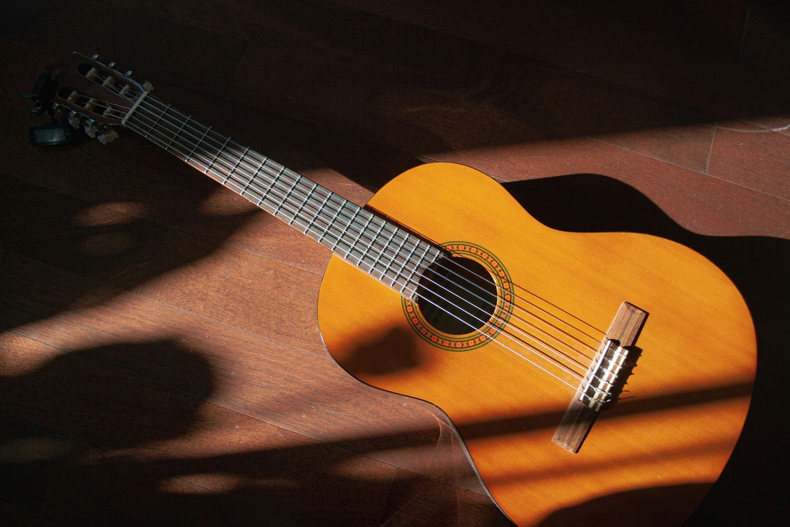 Classical nylon-string guitar on a wooden floor, lit by a strip of warm light