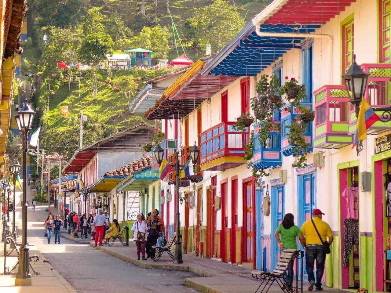 A Quindío coffee-town street at dawn, with brightly painted wooden balconies and mist between the mountains at the far end.