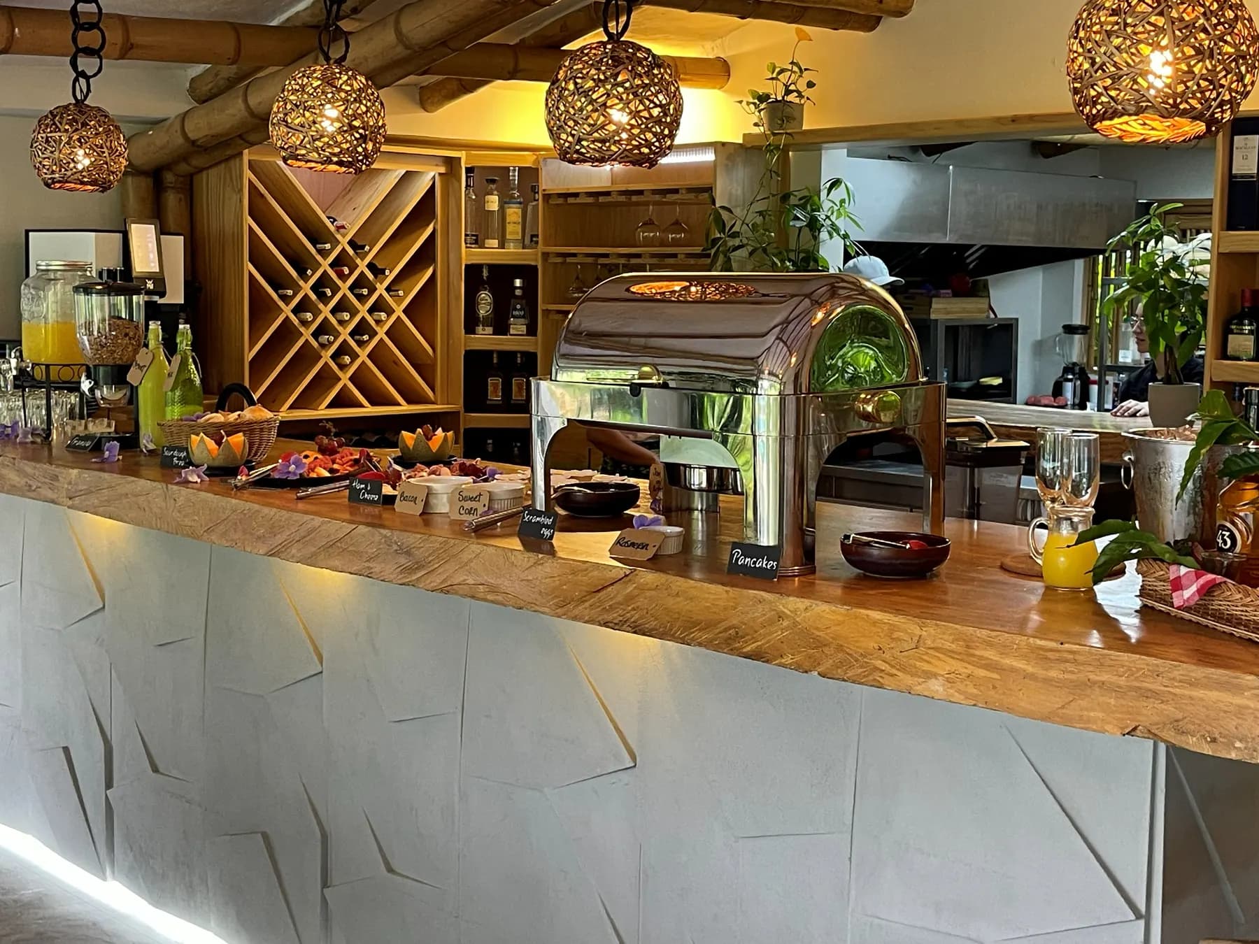 Restaurant counter with a wooden top, a chafing dish, wine shelving and fibre pendant lamps