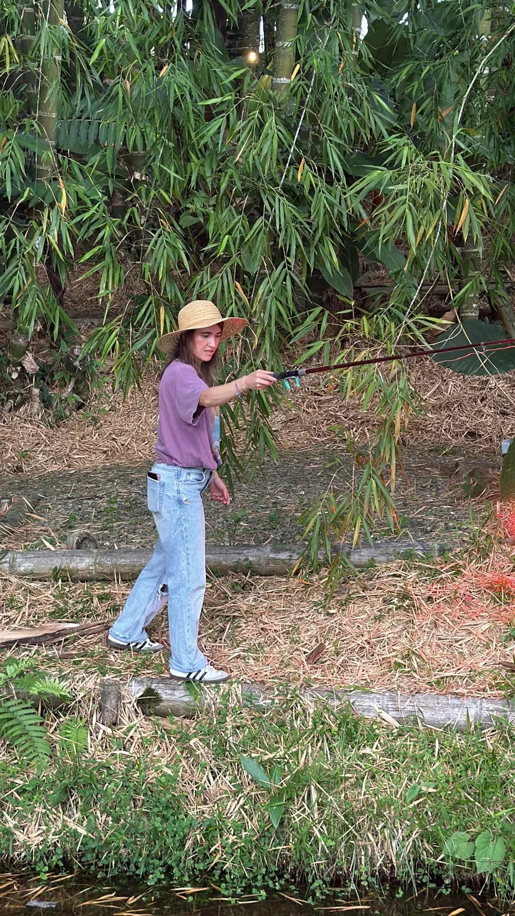 Person standing fishing with a rod beside the lake, among bamboo