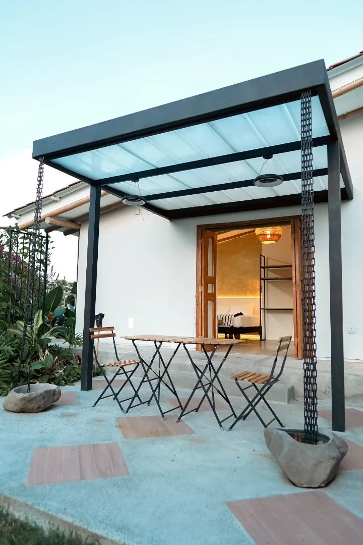 The Dinamita suite pergola with its translucent roof, folding table and chairs, and the door open onto the lit bedroom
