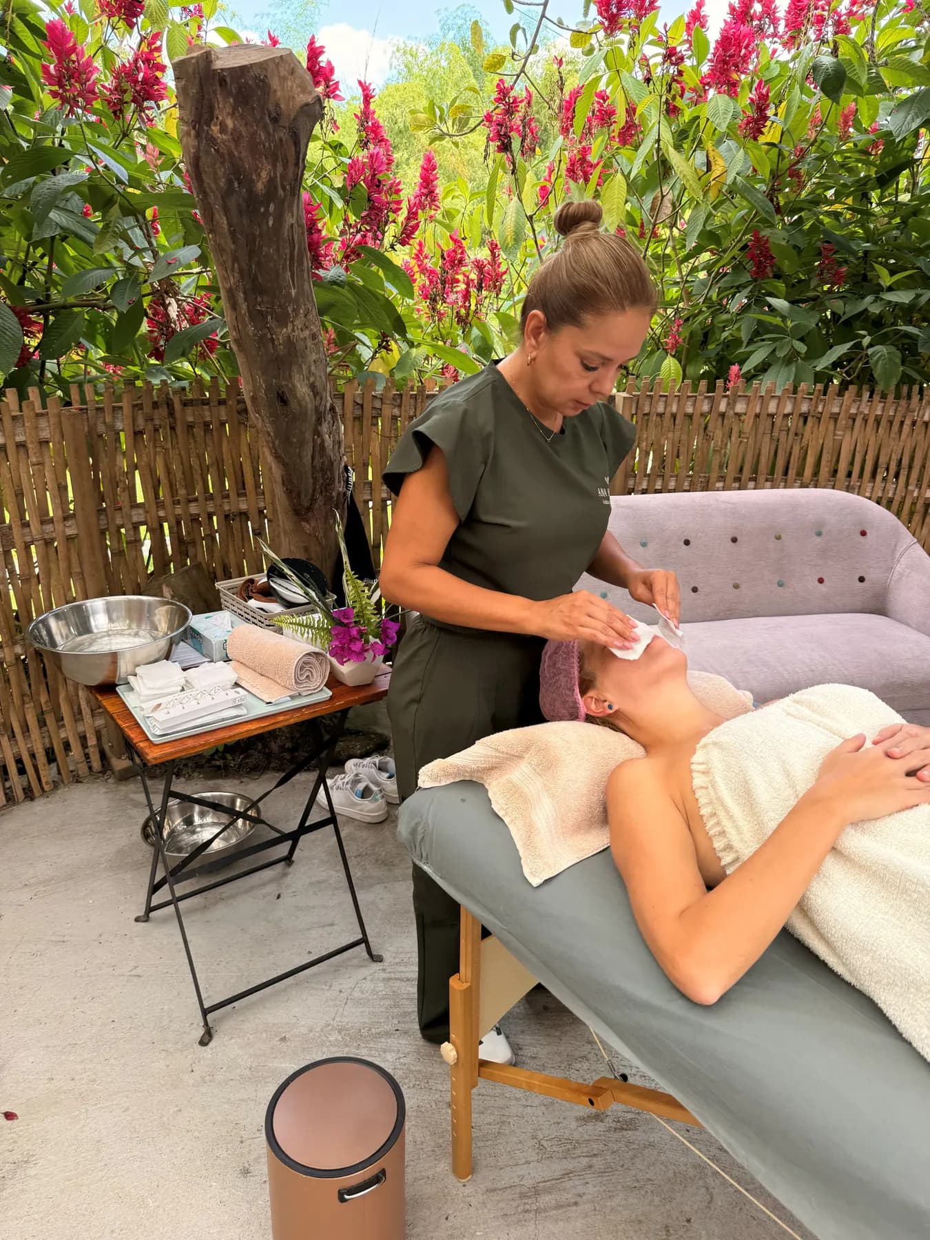 Therapist working on a guest’s legs on an open-air massage table, fuchsia flowers behind